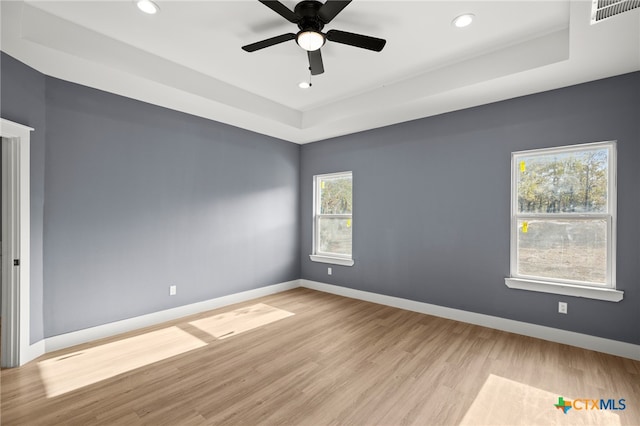 empty room with ceiling fan, light hardwood / wood-style floors, and a raised ceiling