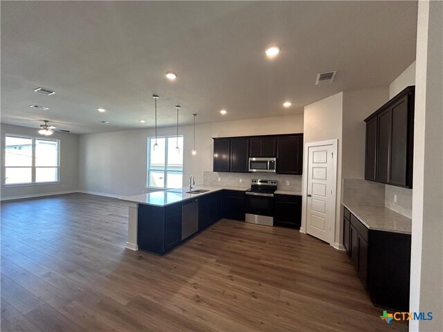 kitchen featuring kitchen peninsula, appliances with stainless steel finishes, hanging light fixtures, dark wood-type flooring, and vaulted ceiling