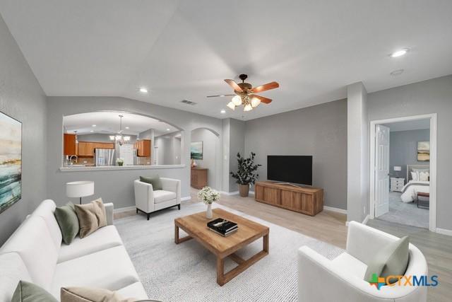 living room featuring ceiling fan with notable chandelier, light hardwood / wood-style floors, and vaulted ceiling