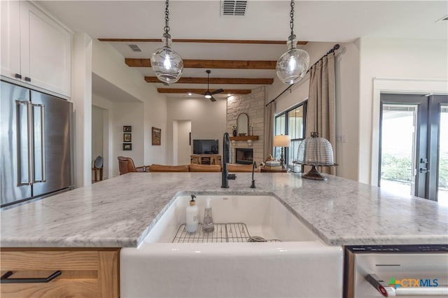 150 Panorama Dr, Wimberley, TX 78676 - kitchen featuring appliances with stainless steel finishes, open floor plan, beam ceiling, a stone fireplace, and light stone countertops