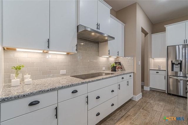 kitchen featuring light stone countertops, stainless steel refrigerator with ice dispenser, black electric stovetop, tasteful backsplash, and white cabinets