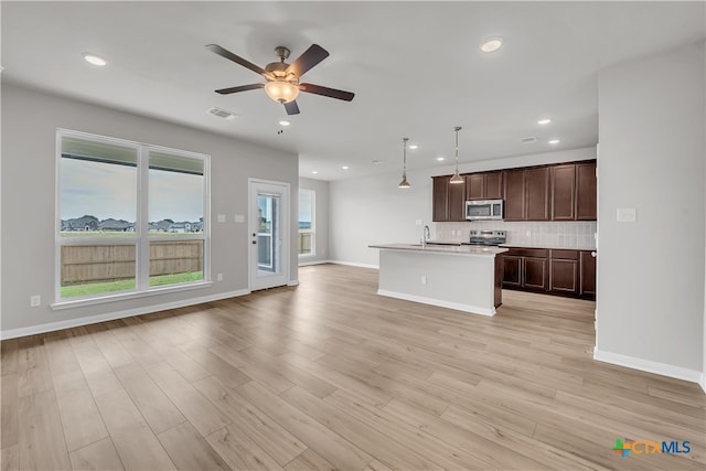 kitchen with decorative light fixtures, an island with sink, light hardwood / wood-style floors, and stainless steel appliances