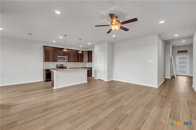 kitchen featuring stainless steel appliances, hanging light fixtures, a kitchen island with sink, backsplash, and light wood-type flooring