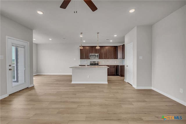 kitchen with stainless steel appliances, sink, hanging light fixtures, an island with sink, and light wood-type flooring