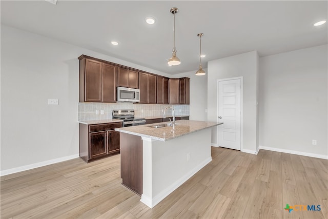 kitchen with a center island with sink, sink, light stone counters, appliances with stainless steel finishes, and light wood-type flooring