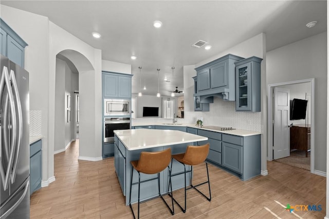 kitchen featuring kitchen peninsula, appliances with stainless steel finishes, tasteful backsplash, a kitchen bar, and a center island