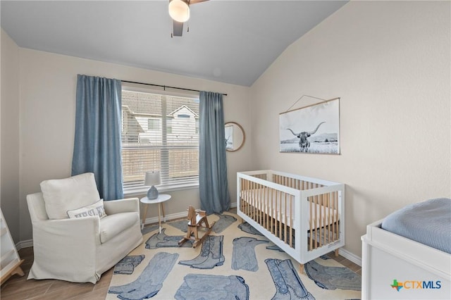 bedroom with ceiling fan, hardwood / wood-style floors, lofted ceiling, and a crib