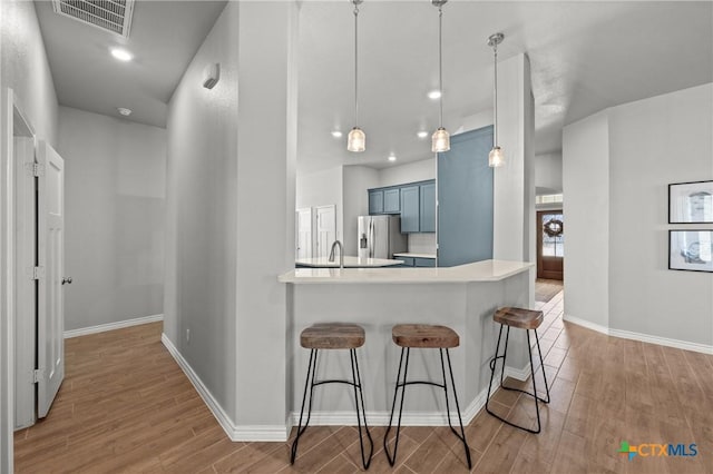 kitchen with blue cabinetry, a kitchen breakfast bar, kitchen peninsula, pendant lighting, and stainless steel fridge