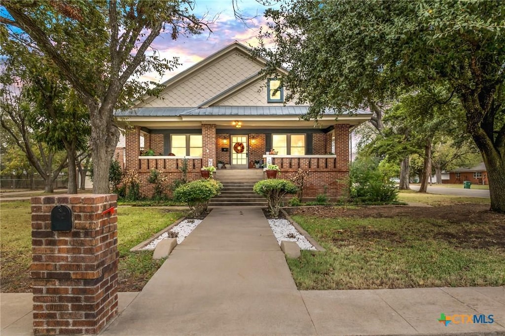 501 S Adams St, Mcgregor, TX 76657 - view of front facade with a standing seam roof, a yard, a porch, metal roof, and brick siding