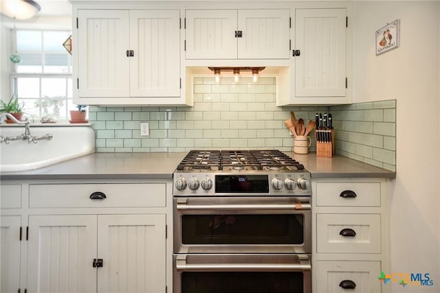 24135 State Highway 172, Port Lavaca, TX 77979 - kitchen with range with two ovens, decorative backsplash, white cabinets, and light countertops