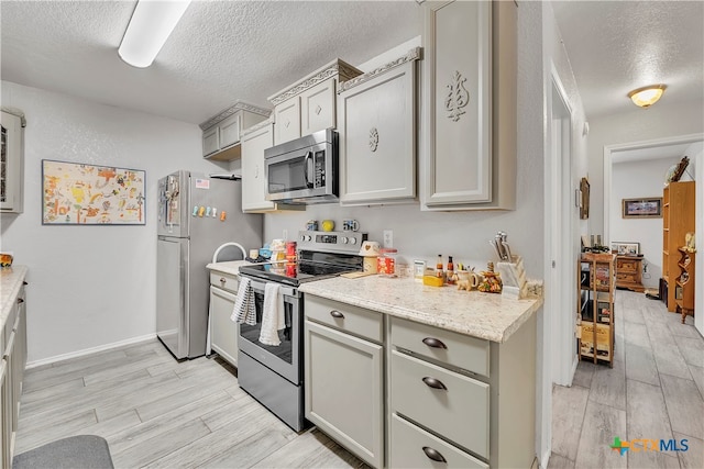 kitchen with stainless steel appliances, gray cabinets, a textured ceiling, and light wood-type flooring