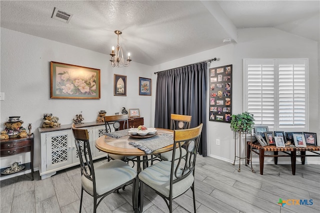 dining room featuring a textured ceiling, light hardwood / wood-style flooring, lofted ceiling, and a notable chandelier