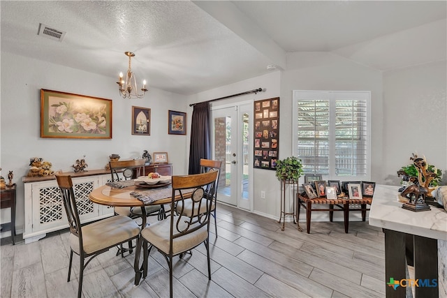 dining room with an inviting chandelier, a textured ceiling, light wood-type flooring, and vaulted ceiling