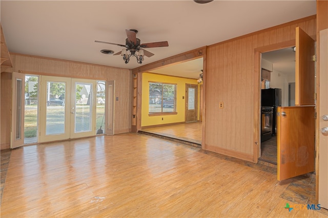 unfurnished room featuring wood walls, light hardwood / wood-style floors, ceiling fan, and french doors