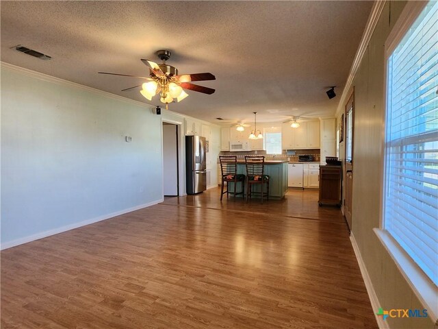 unfurnished living room with crown molding, ceiling fan, dark wood-type flooring, and a textured ceiling