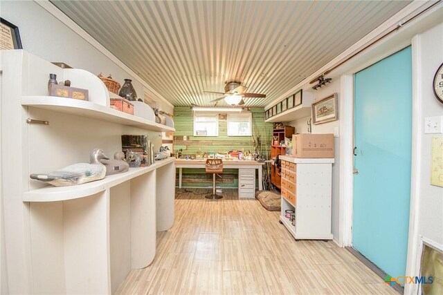 kitchen featuring crown molding, ceiling fan, wooden walls, and built in desk