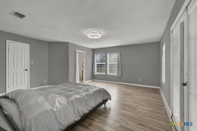 bedroom with wood finished floors, visible vents, and baseboards