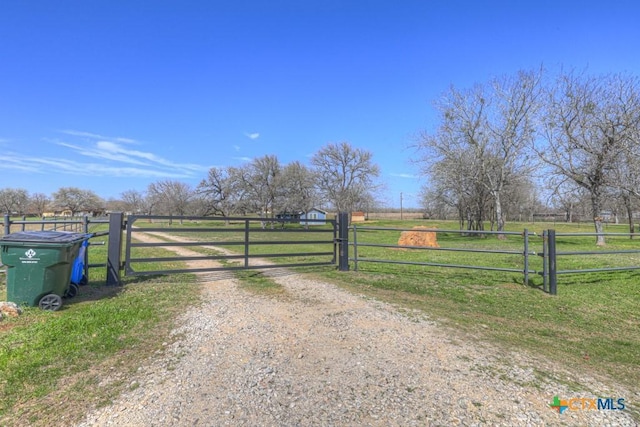 view of gate with a rural view, a lawn, and fence