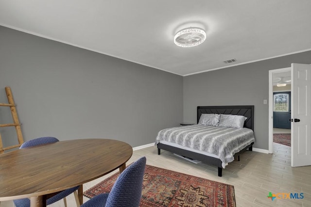 bedroom with light wood-style floors, visible vents, ornamental molding, and baseboards