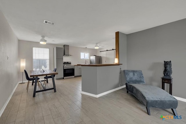 kitchen featuring light wood finished floors, plenty of natural light, visible vents, stainless steel appliances, and wall chimney range hood