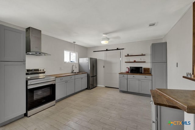 kitchen featuring stainless steel appliances, wooden counters, wall chimney exhaust hood, and a barn door