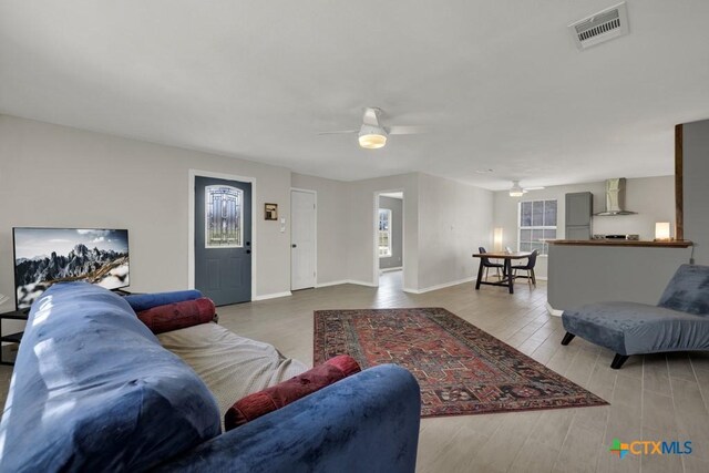 living room with a ceiling fan, visible vents, baseboards, and wood finished floors