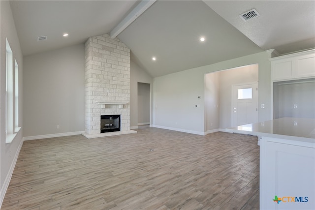 unfurnished living room featuring light wood-type flooring, vaulted ceiling with beams, and a fireplace