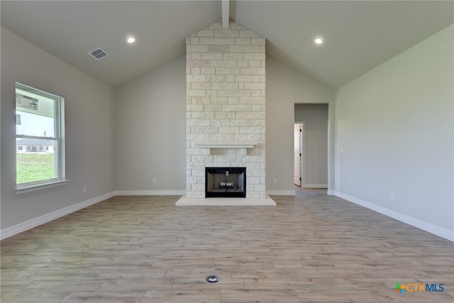 unfurnished living room featuring light hardwood / wood-style floors, a stone fireplace, beam ceiling, and high vaulted ceiling