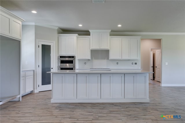 kitchen featuring ornamental molding, white cabinetry, light wood-type flooring, an island with sink, and double oven