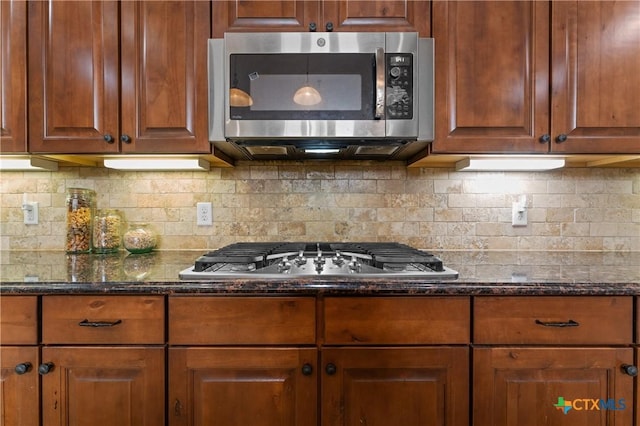 kitchen featuring dark stone counters, stainless steel appliances, tasteful backsplash, and brown cabinetry