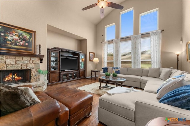 living room with baseboards, wood finished floors, a ceiling fan, high vaulted ceiling, and a stone fireplace