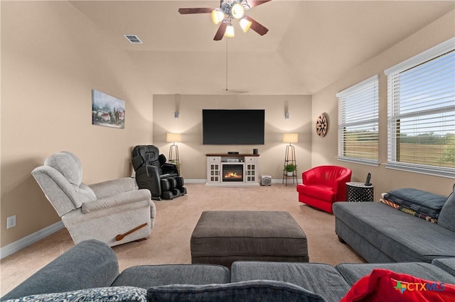 carpeted living room featuring ceiling fan, visible vents, a lit fireplace, baseboards, and lofted ceiling