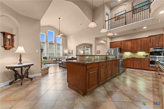 kitchen with a sink, appliances with stainless steel finishes, arched walkways, an island with sink, and a ceiling fan
