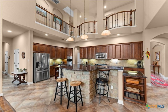 kitchen with dark stone countertops, a breakfast bar, stainless steel appliances, arched walkways, and a large island