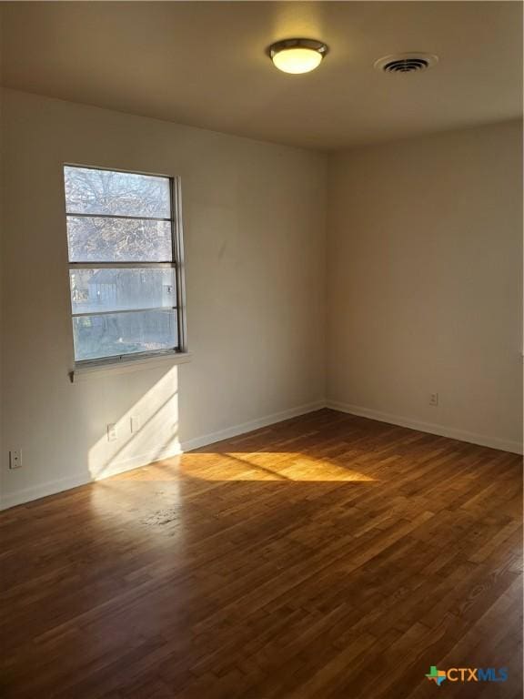 unfurnished room with dark wood-type flooring, visible vents, and baseboards