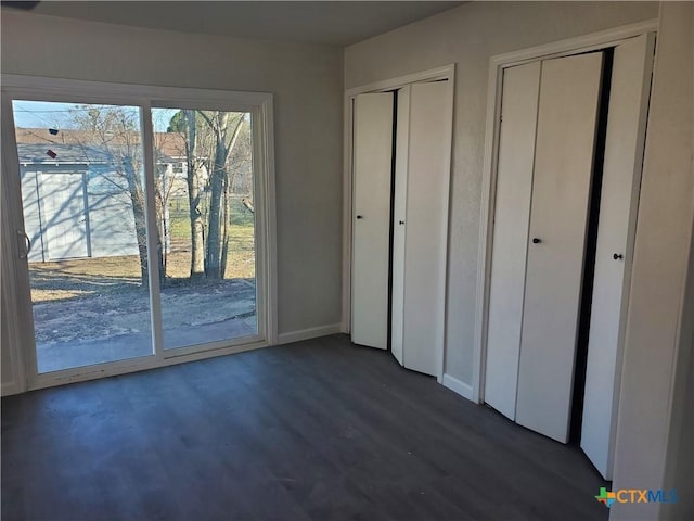 unfurnished bedroom featuring access to outside, baseboards, two closets, and dark wood finished floors