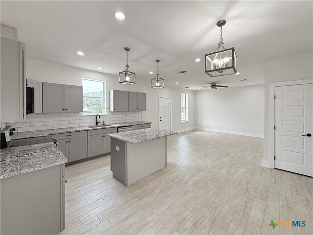 1637 Bob White Dr, Spring Branch, TX 78070 - kitchen featuring gray cabinets, a ceiling fan, a kitchen island, tasteful backsplash, and plenty of natural light