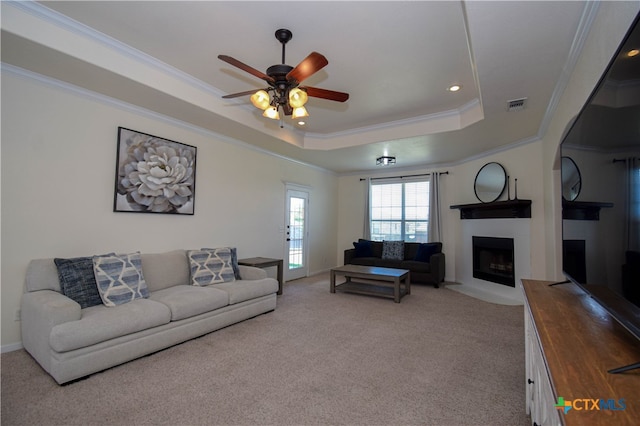 carpeted living room with ceiling fan, crown molding, and a raised ceiling