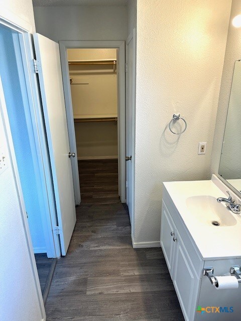 4505 Mustang Dr, Killeen, TX 76549 - bathroom with baseboards, wood finished floors, a textured wall, vanity, and a walk in closet