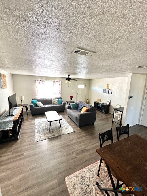 living room featuring hardwood / wood-style flooring, ceiling fan, and a textured ceiling