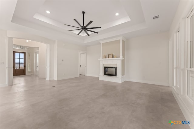 unfurnished living room featuring a raised ceiling, visible vents, finished concrete floors, a glass covered fireplace, and ceiling fan