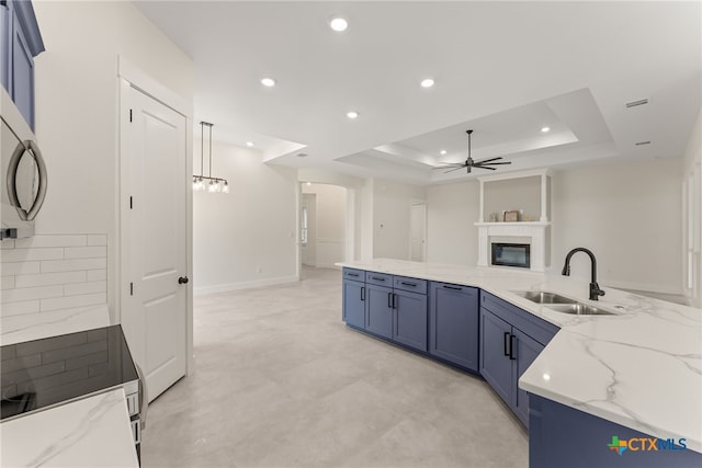 kitchen featuring blue cabinetry, a raised ceiling, a sink, and a glass covered fireplace