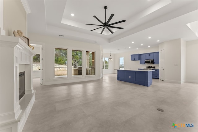 unfurnished living room with a glass covered fireplace, ceiling fan with notable chandelier, a tray ceiling, a sink, and recessed lighting