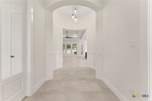 hall featuring baseboards, arched walkways, a decorative wall, and a tray ceiling