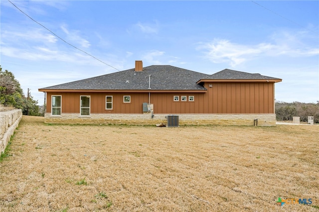 back of property with central AC, a yard, a chimney, and stone siding