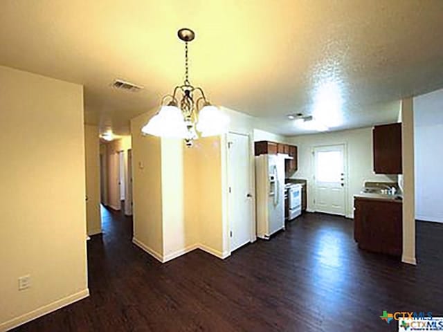 kitchen with a textured ceiling, dark wood-type flooring, white appliances, and an inviting chandelier