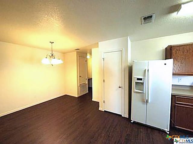 kitchen with a textured ceiling, white fridge with ice dispenser, a chandelier, dark hardwood / wood-style floors, and hanging light fixtures