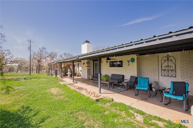 rear view of property with brick siding, a chimney, a yard, a ceiling fan, and a patio