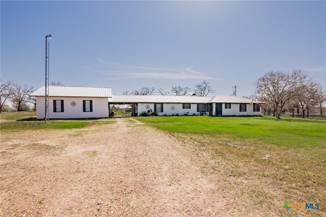 ranch-style home featuring metal roof, a front yard, an attached carport, and dirt driveway