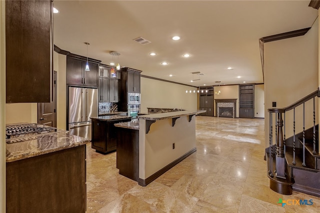 kitchen with stainless steel appliances, decorative light fixtures, light stone countertops, a tile fireplace, and a center island